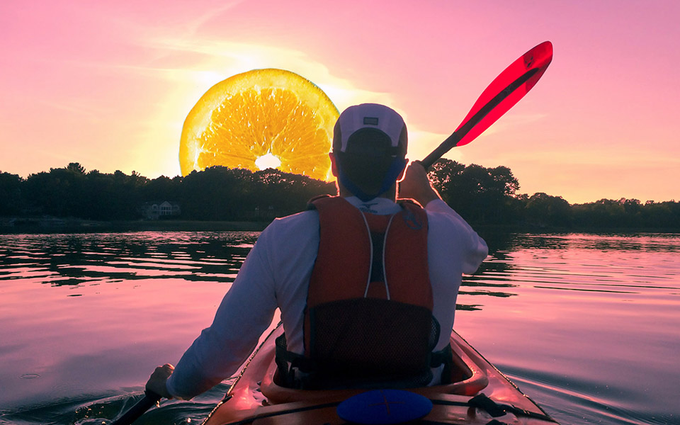 Photo of a person canoeing towards the sun, but the sun is a slice of orange.